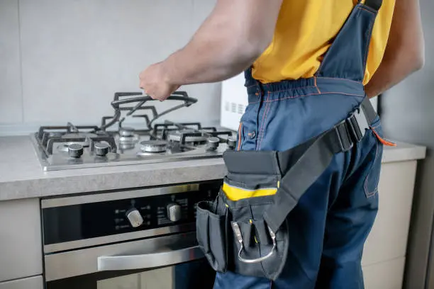 Technician adjusting gas stove burners in modern kitchen, emphasizing professional appliance repair services by Fulgor Milano in Toronto.