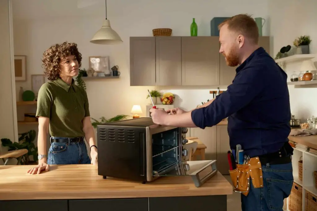 Technician diagnosing a broken microwave with a customer in a modern kitchen, showcasing professional appliance repair services in Brampton.