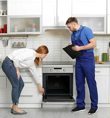 Technician inspecting oven with homeowner in modern kitchen, highlighting appliance repair service and customer interaction.